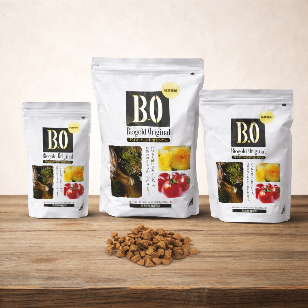 Three bags of Boogold Original bonsai fertiliser on a wooden surface with scattered fertiliser pellets. 900 grams and 2.4 kilograms and 5 kilograms.